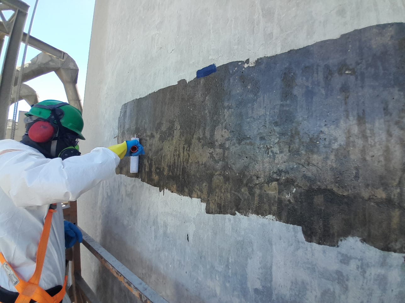 Profissional com capacete, proteção respiratória, luvas e cinturão trabalhando na superfície do silo